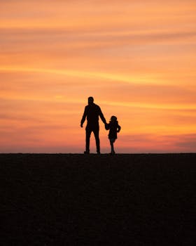 Silhouette of a father and daughter walking hand in hand during a vibrant sunset in Brighton.